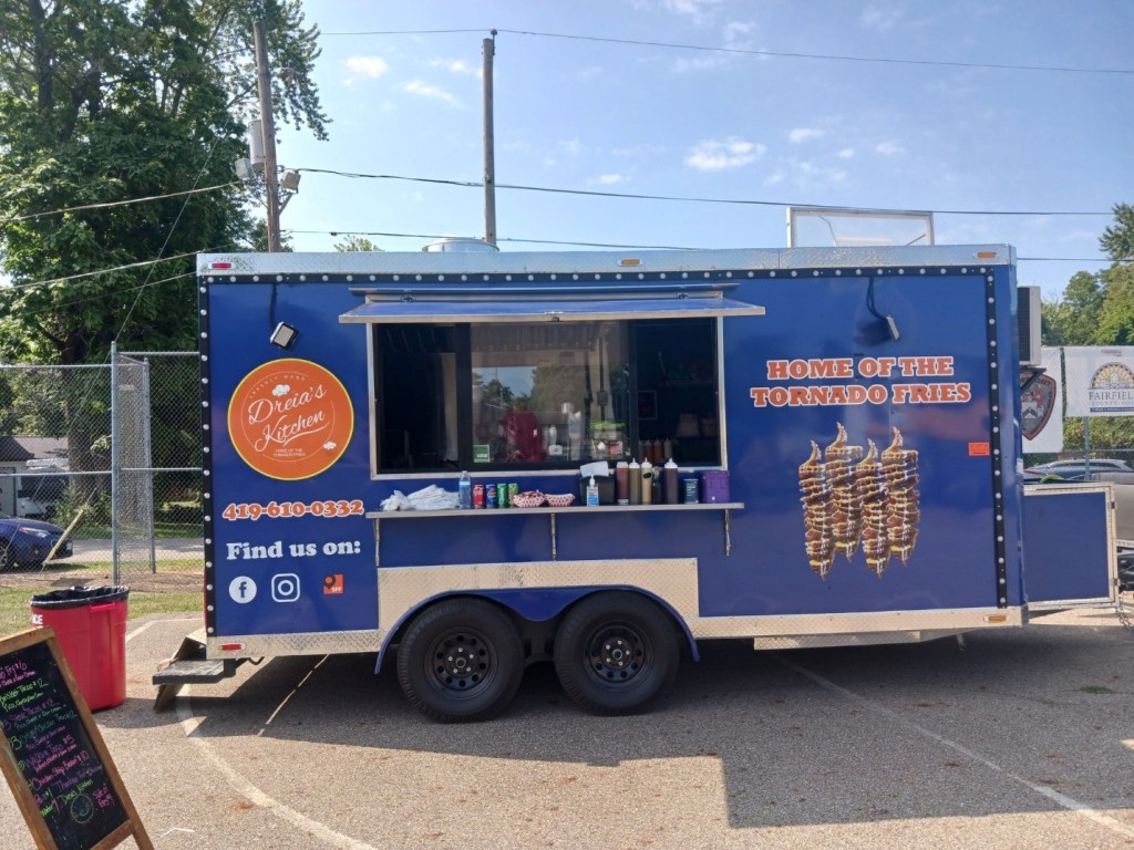 Food truck with blue exterior and a sign stating 'Home of the Tornado Fries' and 'Dreia's Kitchen' prominently displayed, featuring a window serving area.